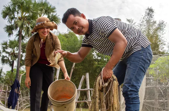 Staff members from MCC partner Organization to Develop Our Villages (ODOV) Hat Sinet and Nov Dina, take fish from a net they caught in a fishpond at the farm of ODOV farmer Mok Samun. ODOV is teaching beneficiaries how to become more resilient in the face of climate change. 