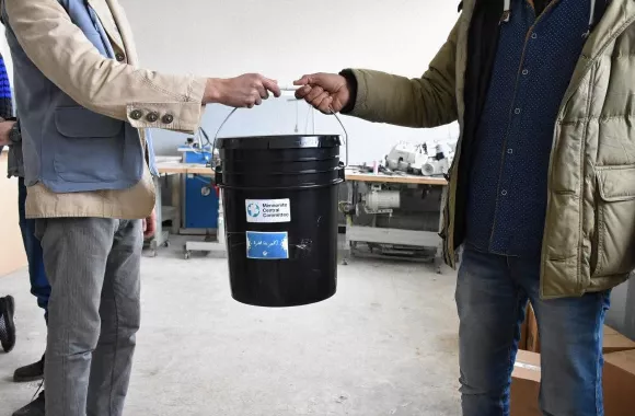 A person hands another person a 5 gallon bucket.