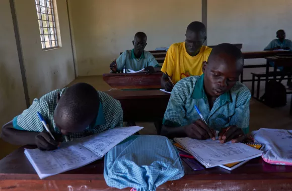 Two South Sudanese students write in notebooks while sitting at a desk