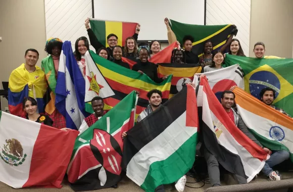 A large group of young adults pose for photo. They are holding different country flags.