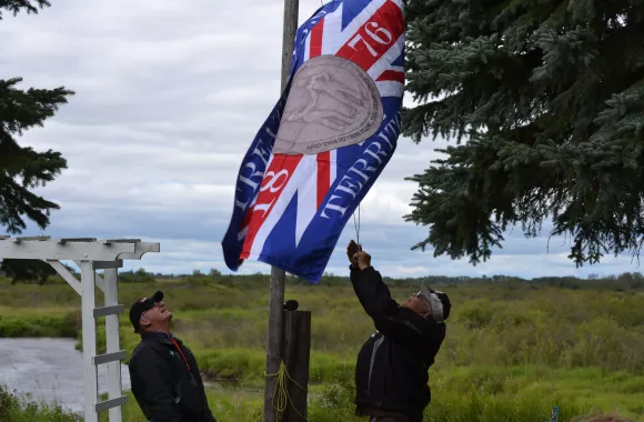 Two men in hats and jackets raise a flag on a flag poll