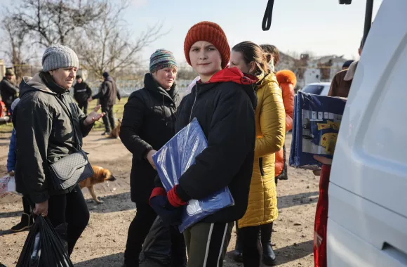 A young person in Ukraine carrying bedding they received from MCC
