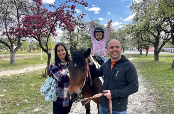 A man and woman next to a horse with a child on it