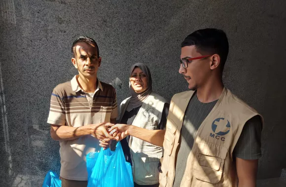 A man and woman handing relief supplies to a man in Gaza