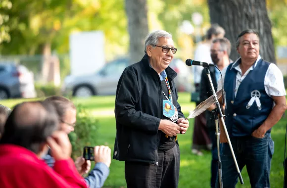 A man speaking into a mic in front of a group of people in a park