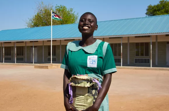 A girl standing outside of a school holding a school kit