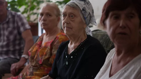 Three elder, Ukrainian women. The middle woman has a scarf on her head.