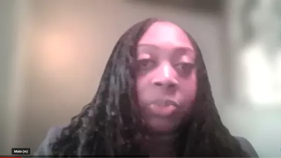 A woman with long hair speaks into the camera on a video call