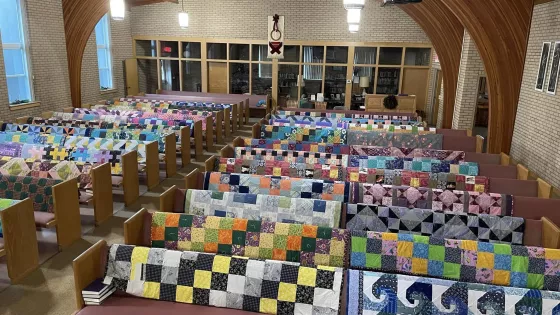 50 colorful comforters draped over church pews