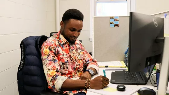 A young man in a floral shirt sits in front of a computer