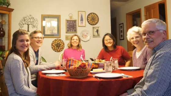 A group of six people sit around a dining room table. They are all smiling at the camera.