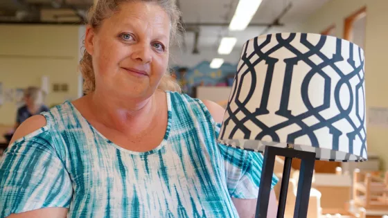 Woman with blue and white dress holds a refurbished lamp.