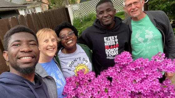 Three young adults from Africa take a photo with their host parents from the United Stated. They are standing behind a pink flowering bush.