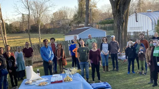 A group of people stand facing the camera in a backyard with a table of treats in the foreground.