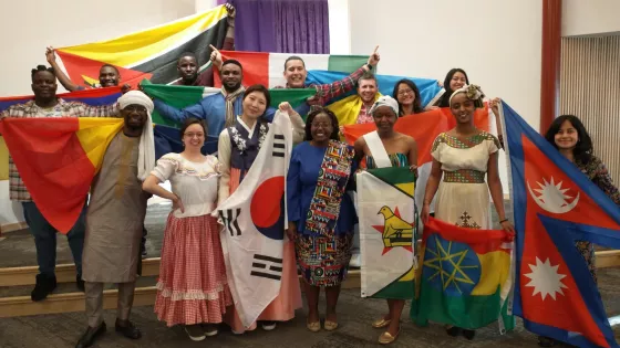 A group of young adults of different nationalities stand together. They are holding their country flags and dressed in traditional outfits.