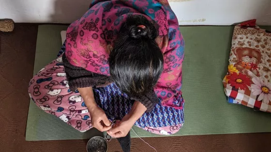 Woman sitting on a mat threading a needle.