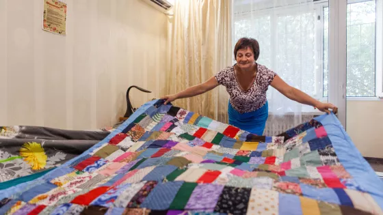 A Ukrainian woman places a colorful comforter over a bed