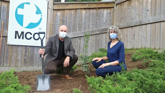 A man and woman planting a tree in front of an MCC sign