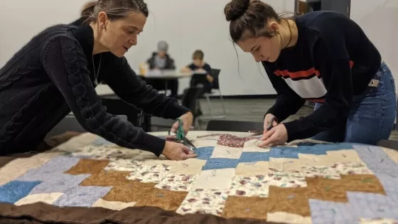 Two women lean over a comforter top they are working on.