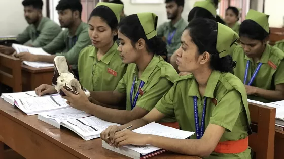 Nursing students sit at tables in a school classroom