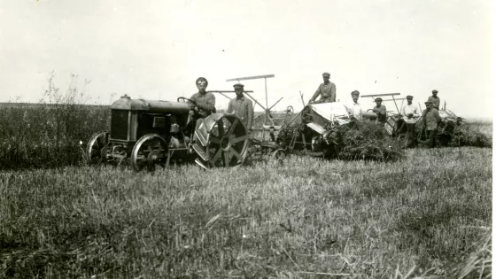 A black and white photo from the 1920s of farmers in a field with tractors