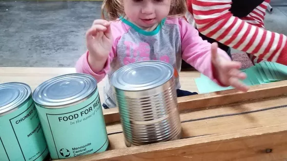 A young girl pushes cans down a wooden conveyer