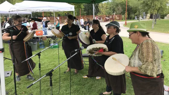 A group of Indigenous women play hand drums at an outdoor event