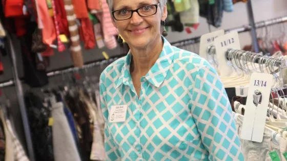 An older woman with short hair stands in the clothing section at a Thrift Shop