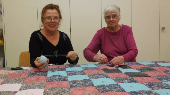 Two women sit and tie a comforter top