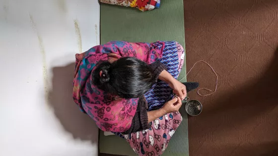 A woman sitting on a floor beading a necklace.