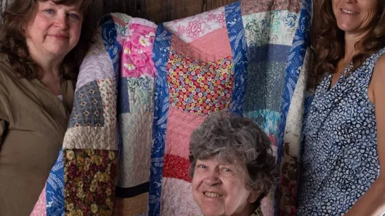Three women pose with a quilt