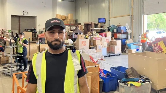 A man in a high-visibility vest stand in front of a warehouse full of boxes