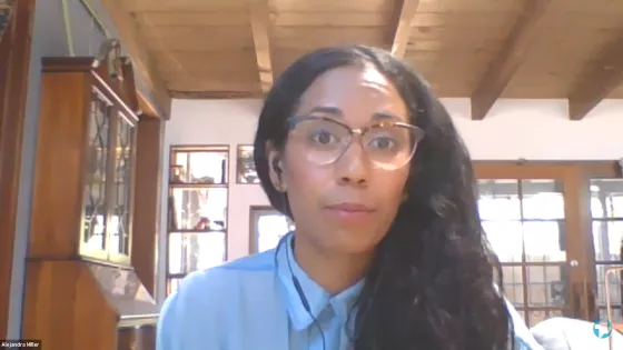 Woman with glasses and brown hair speaks from dining room.