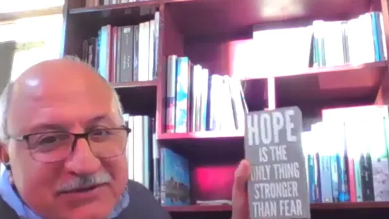 man holding sign "Hope is the only thing stronger than fear" in front of bookshelf