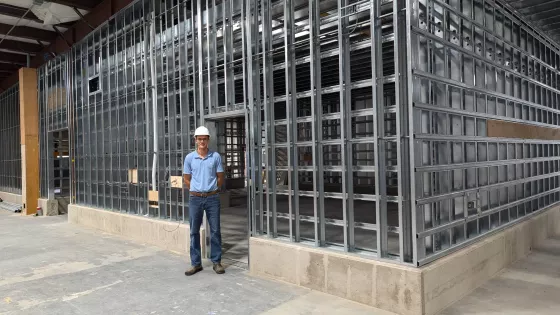 man in hard hat stands in front of a wall of steel studs under construction