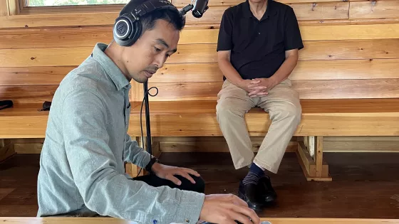 Man in green shirt adjusts sound recording while man in black shirt waits beside a microphone