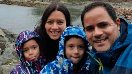 A picture of a family of four: a mother, father, son and daughter in front of a body of water and trees in the backgorund