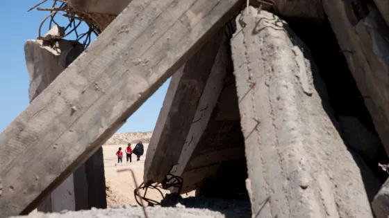 people walking in desert behind bombed cement structure