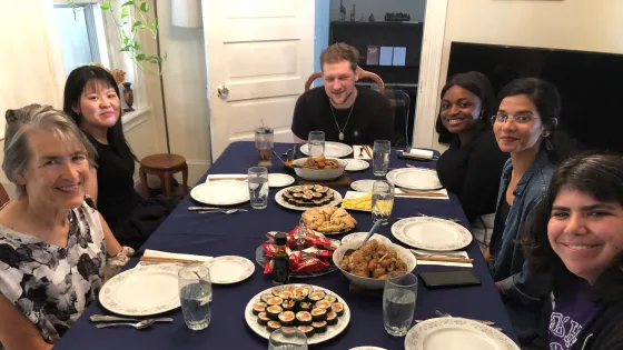 Six people sit around a table set with various plates of Korean food.