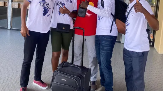 Five people stand outside the Beira International Airport. The four people flanking the person in center are wearing t-shirts that say "welcome."