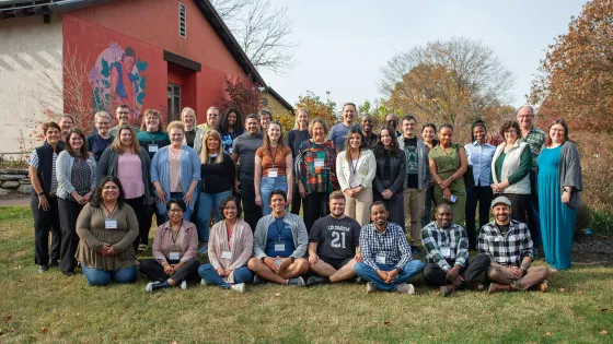 A diverse group of about 40 people stand in rows and sit on the grass.