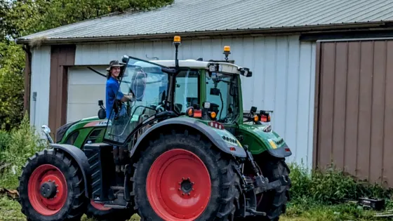 A person stands on the steps to an enormous tractor.