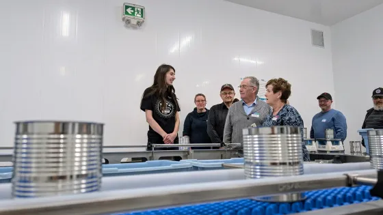 A woman explains how a piece of equipment in the MCC Meat Cannery works.