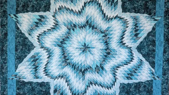 A blue quilt in a star pattern with waves woven between the points.