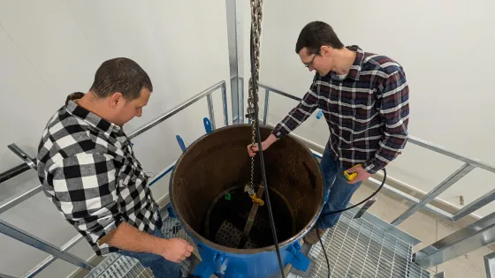 Two men look into a large round metal container. 