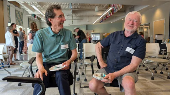 Two men sit beside each other laughing.