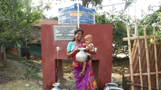 Churki Tudu of India and her daughter Promila stand in front of a submersible pump as they draw clean water from it.