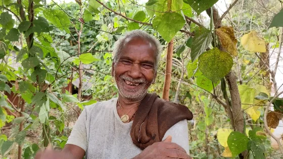 Parma Bardaset, a farmer from Bhutadi, India smiles as he stands in front of bean plants he grew in his kitchen garden.