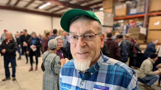 A older man wears a plaid shirt, hat, and glasses at the grand opening of the stationary cannery.