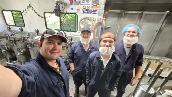 four men standing in a row pose for selfie with metal equipment in the background